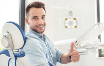 A satisfied young man in a dental chair showing his thumb up .