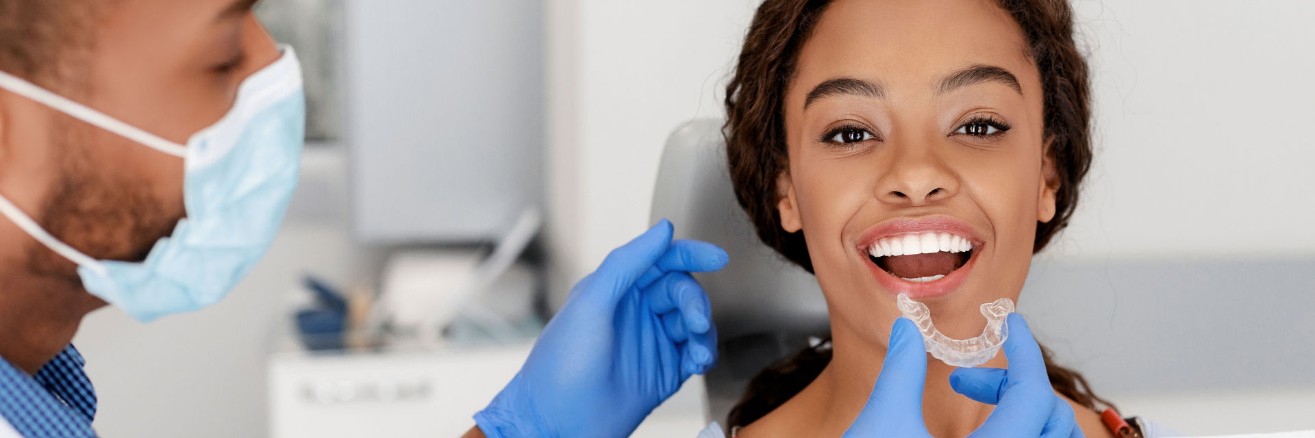 A woman with perfect teeth sitting in a dental chair and an orthodontist with a clear aligner checking the effects of the orthodontic treatment.