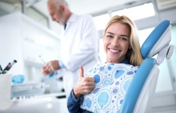 Asatisfied woman with a perfect smile sitting in a dental chair and showing her thumb up.
